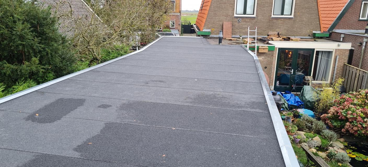 Lang afgewerkt bitumen dak met zinken randen achter een woning met tuin
