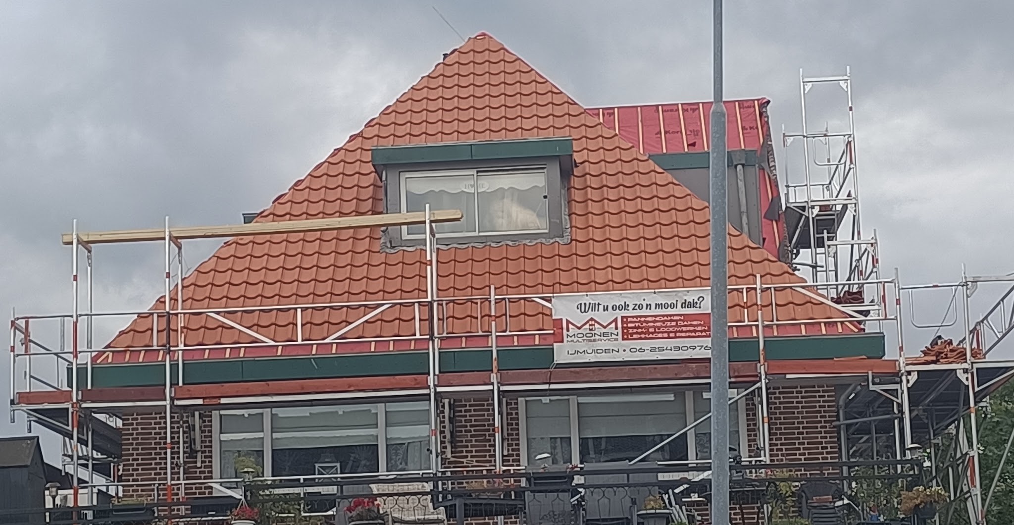 Woning met nieuw oranje pannendak in de steigers, met het spandoek van Moonen Multiservice