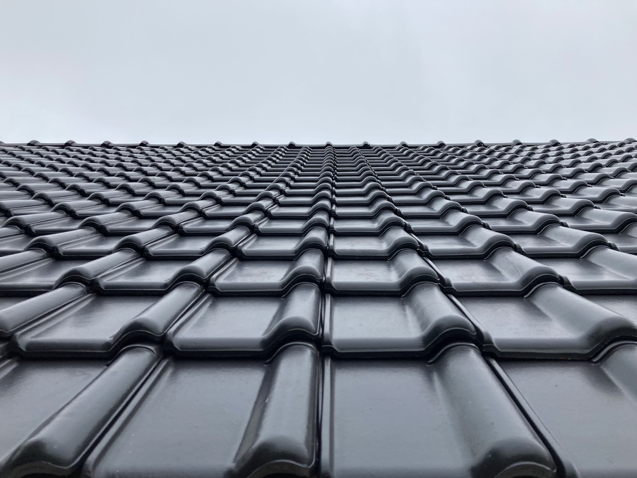 Nieuwe glanzend zwarte dakpannen tegen een grijze lucht